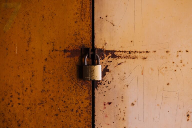 Zero Trust Security Model Explained for Sysadmins A close-up view of a rusty padlock securing a weathered metal door, highlighting decay and security.