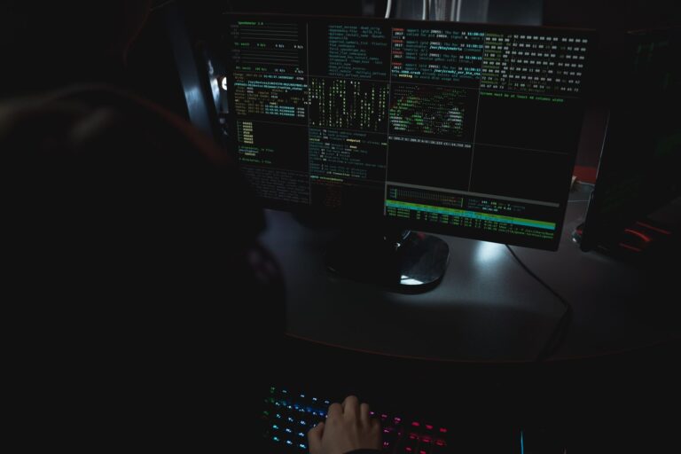 Ransomware Defense Strategies for Small IT Teams Dark room setup with code displayed on PC monitors highlighting cybersecurity themes.