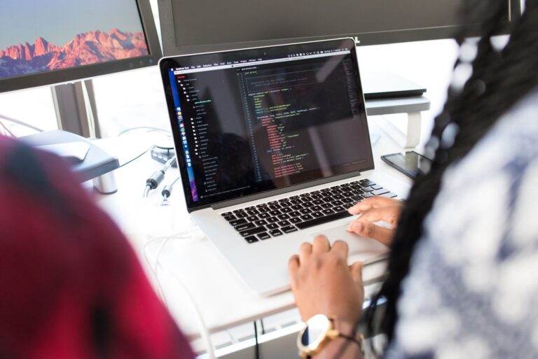 Best Cloud Monitoring Tools for DevOps Teams A woman coding on a laptop in a modern office environment with multiple monitors.